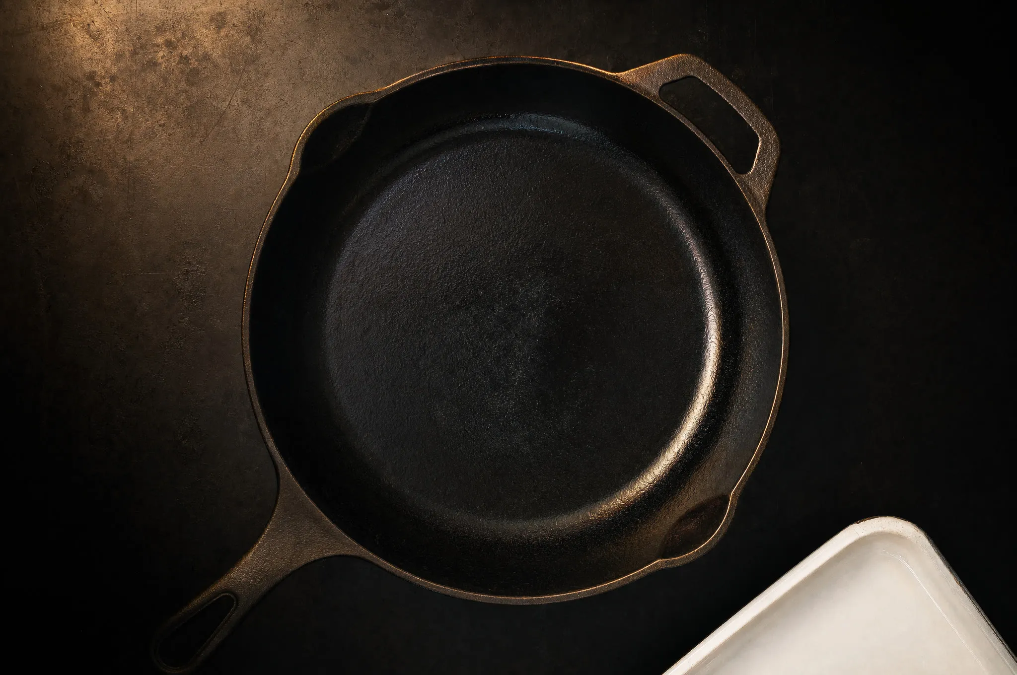 Modern pebbly-surfaced cast iron skillet beside a glass-smooth vintage one in raking light