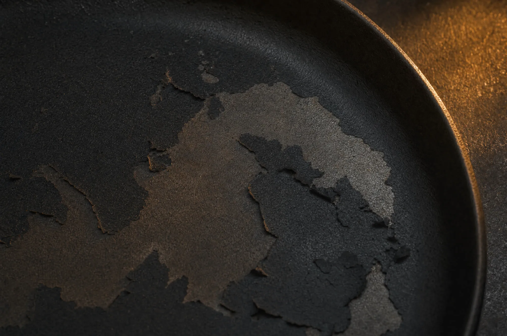 Cast iron skillet surface with patches of seasoning flaking and peeling, gray iron showing beneath