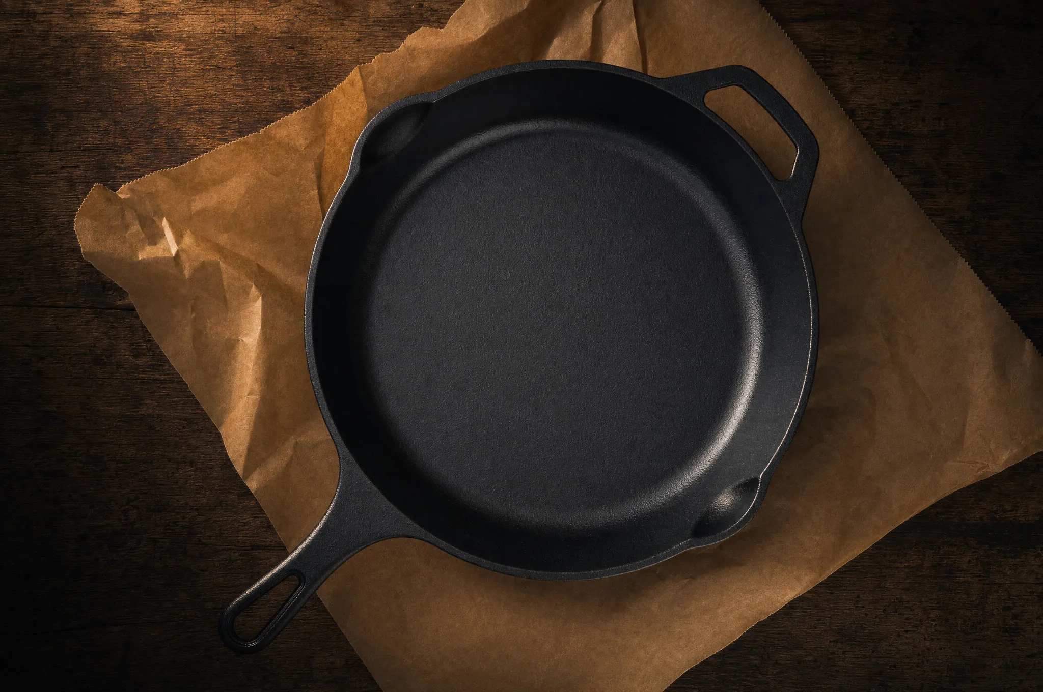 Brand-new matte black cast iron skillet on butcher paper on a wooden counter